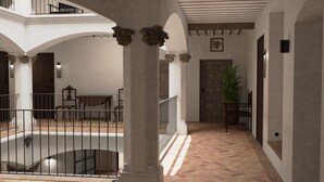 A spacious interior with a high ceiling, a central column with ornate capitals, a tiled floor, and a door with a decorative panel. - Hotel Boutique Casona de los Rebolledo (Zújar)
