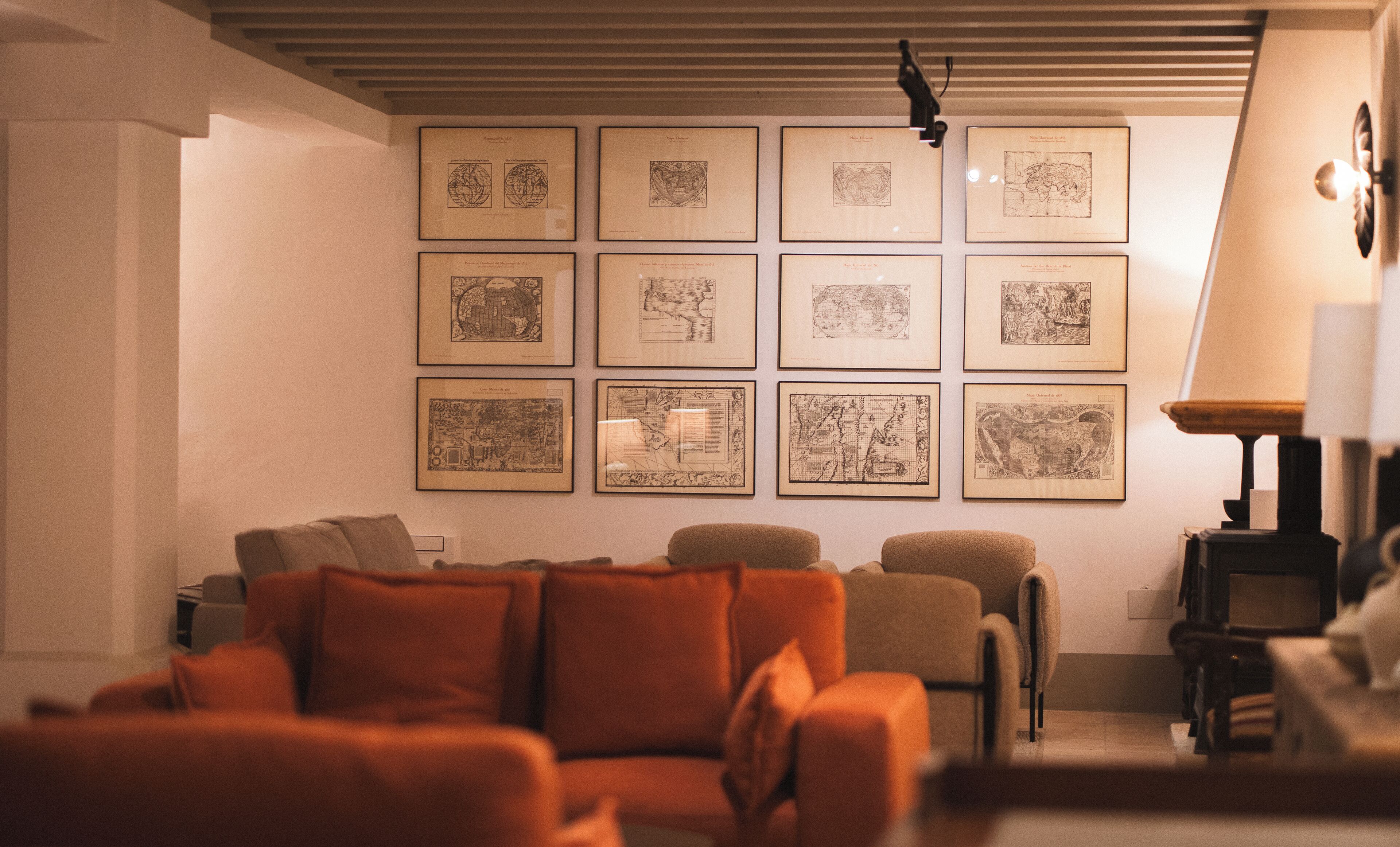 Een woonkamer met een bank, een lamp en lijstjes met kaarten aan de muur.