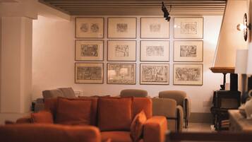 Een woonkamer met een bank, een lamp en lijstjes met kaarten aan de muur.