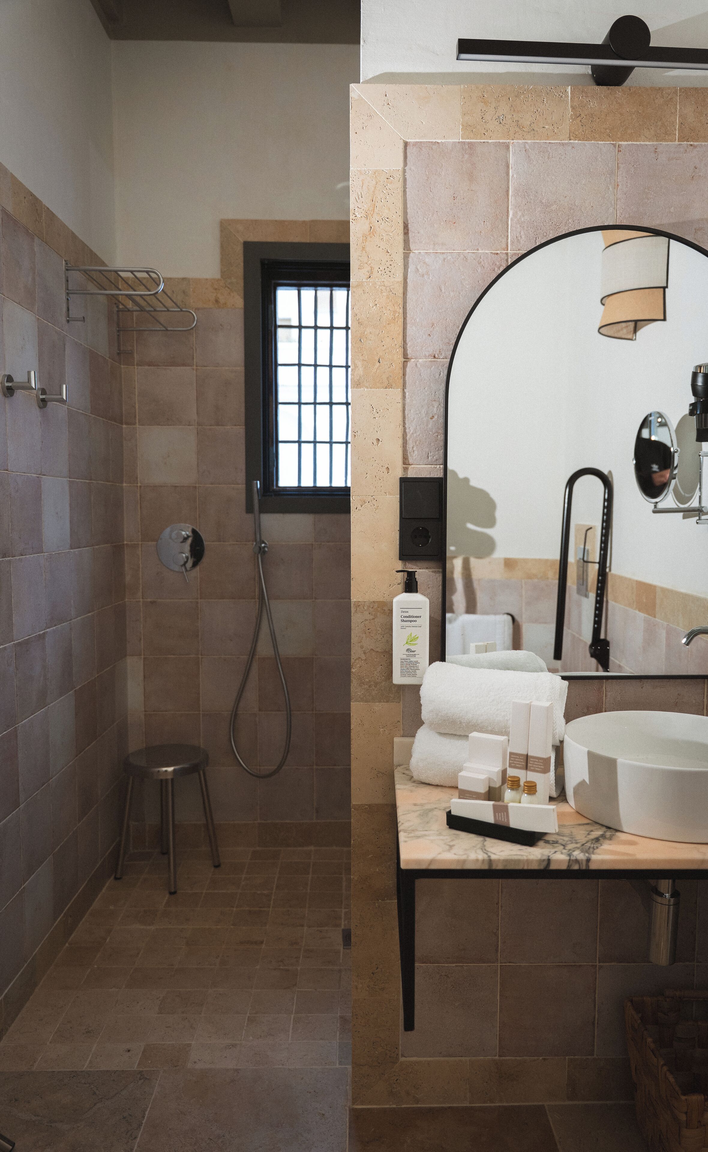 Un baño con ducha, lavamanos, espejo y artículos de aseo.