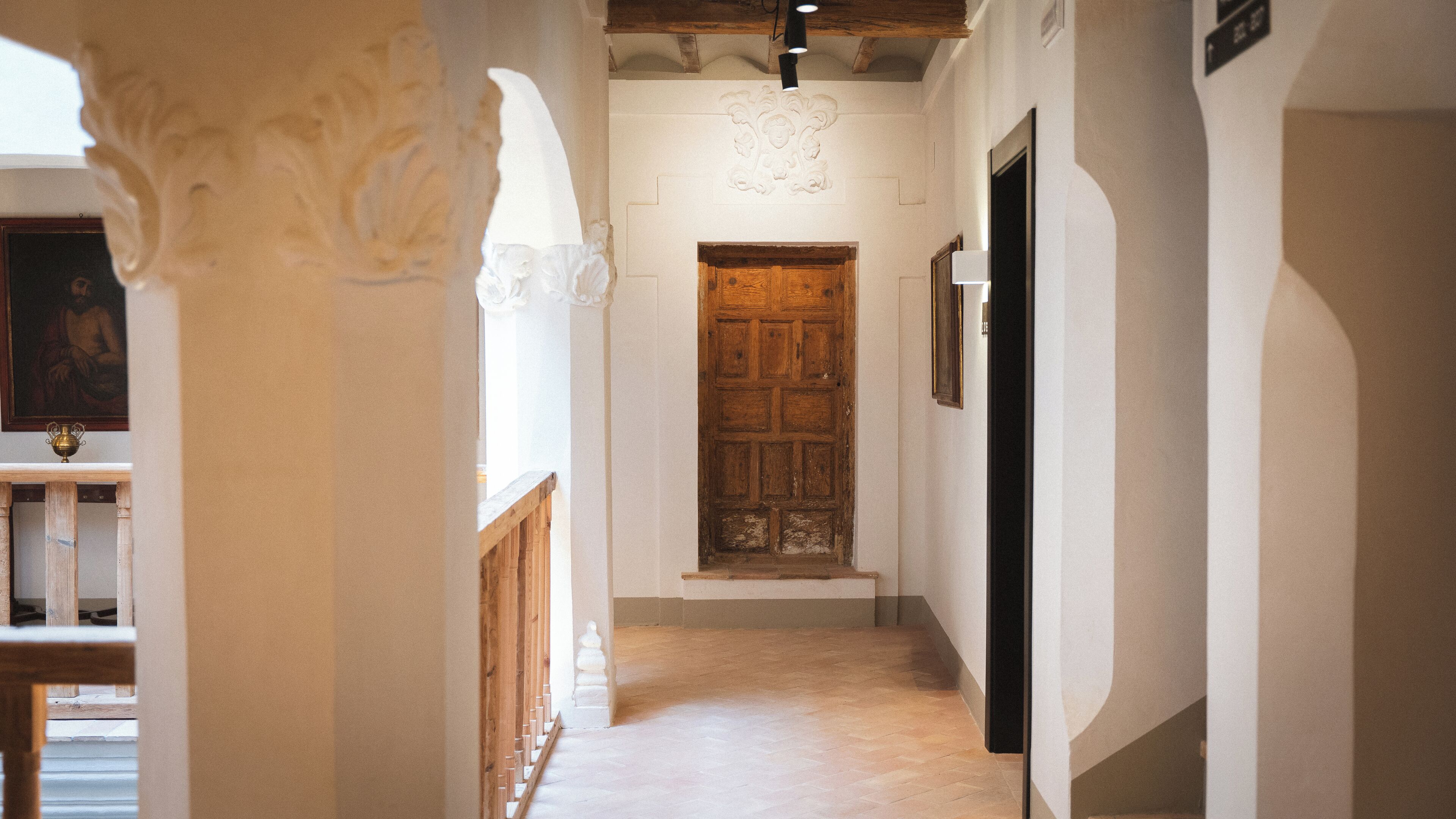 A hallway with a wooden door, white walls, and a wooden railing.