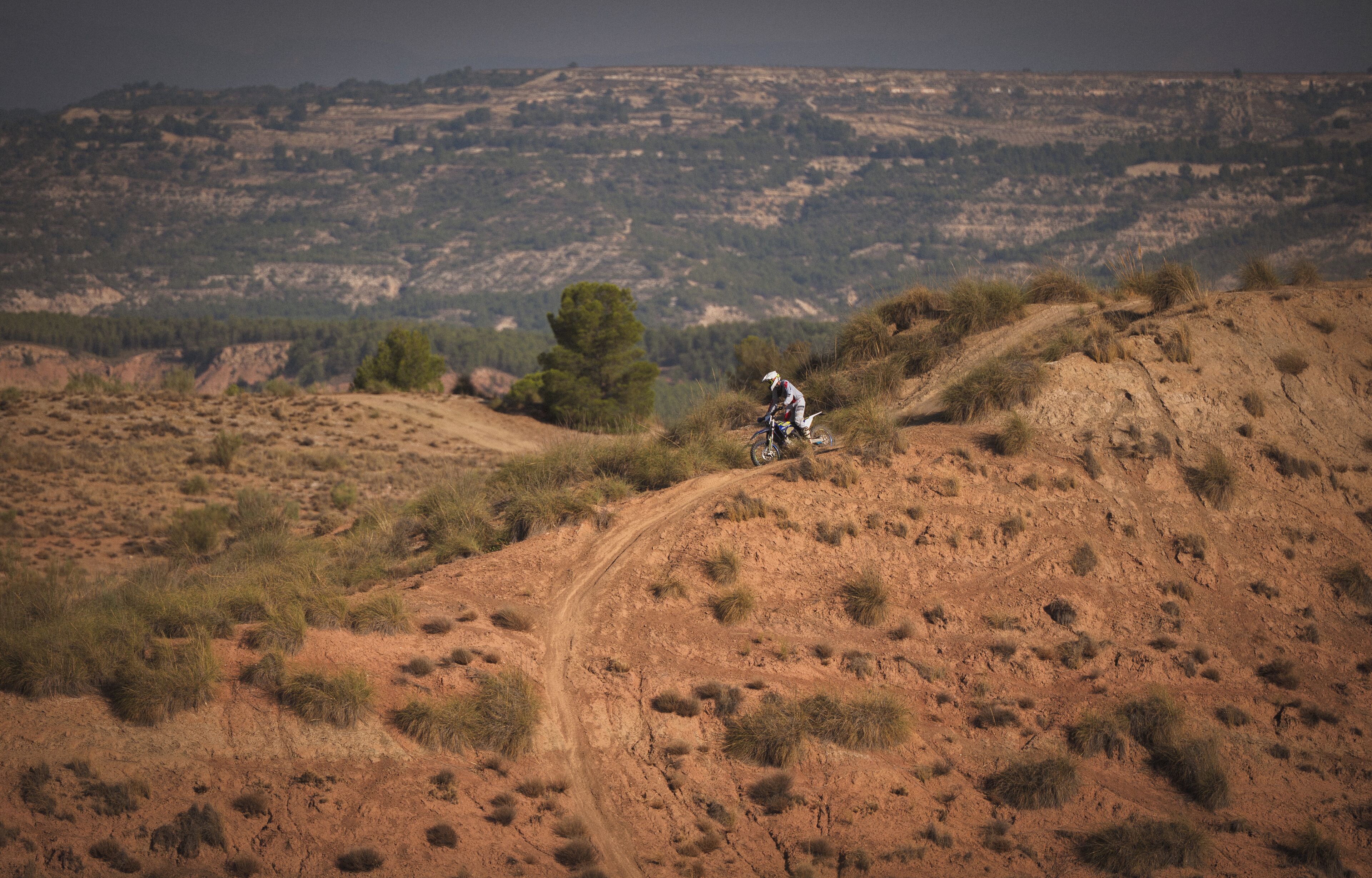 A dirt bike trail winding through a hilly, grassy landscape with sparse trees.
