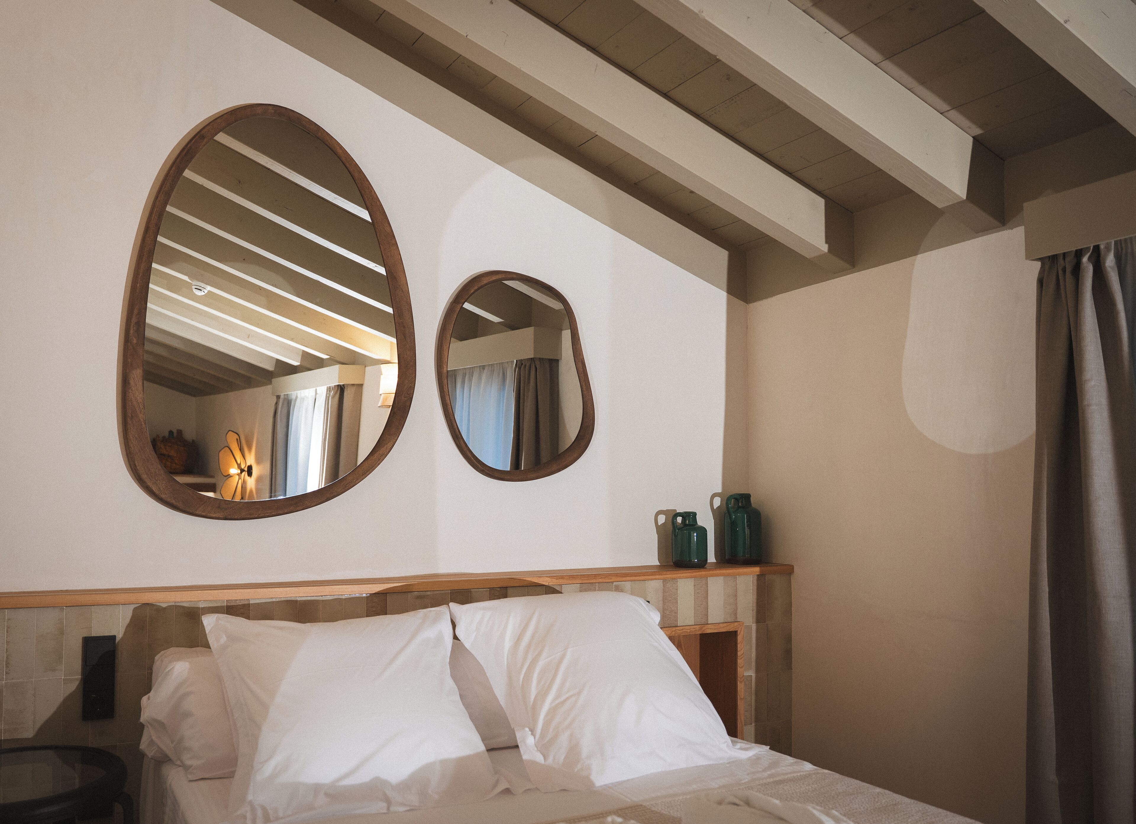 Ein Hotelzimmer mit einem Bett, zwei Wandspiegeln, einem Holzkopfende und einem kleinen Tisch mit einer Lampe.