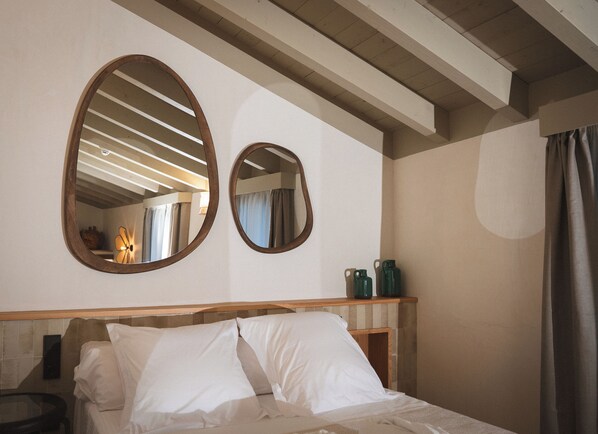 A hotel room with a bed, two wall mirrors, a wooden headboard, and a small table with a lamp.
