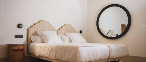 Un dormitorio con una cama, una mesita de noche, un espejo redondo y una araña.