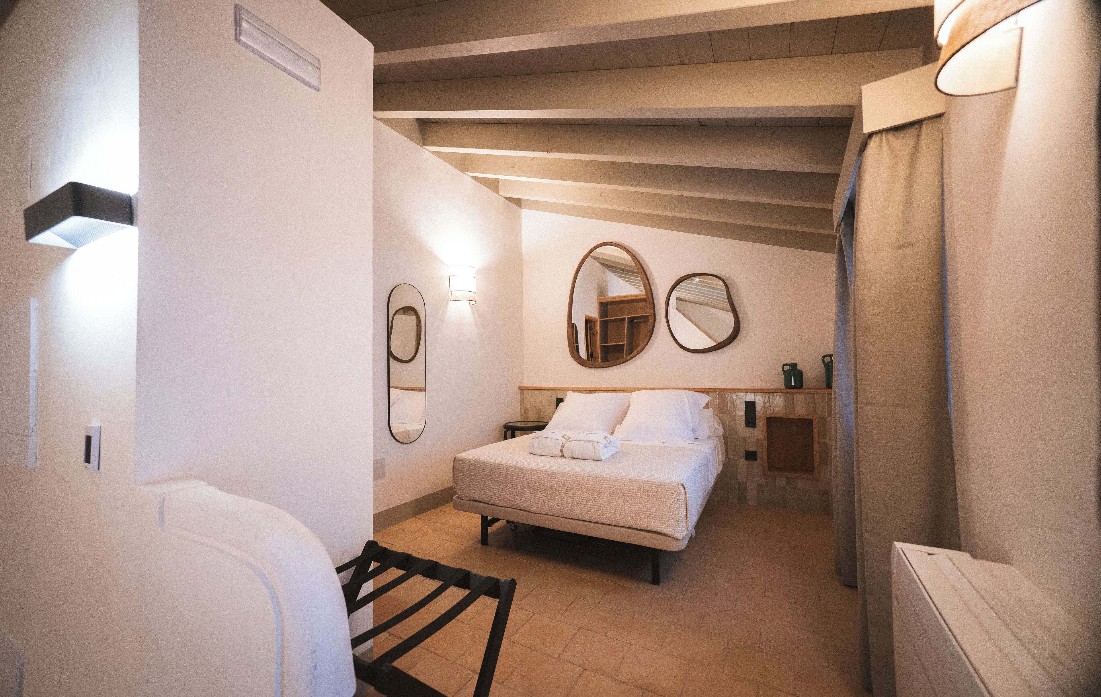 Una habitación de hotel con cama, mesitas de noche, un espejo y una ventana.