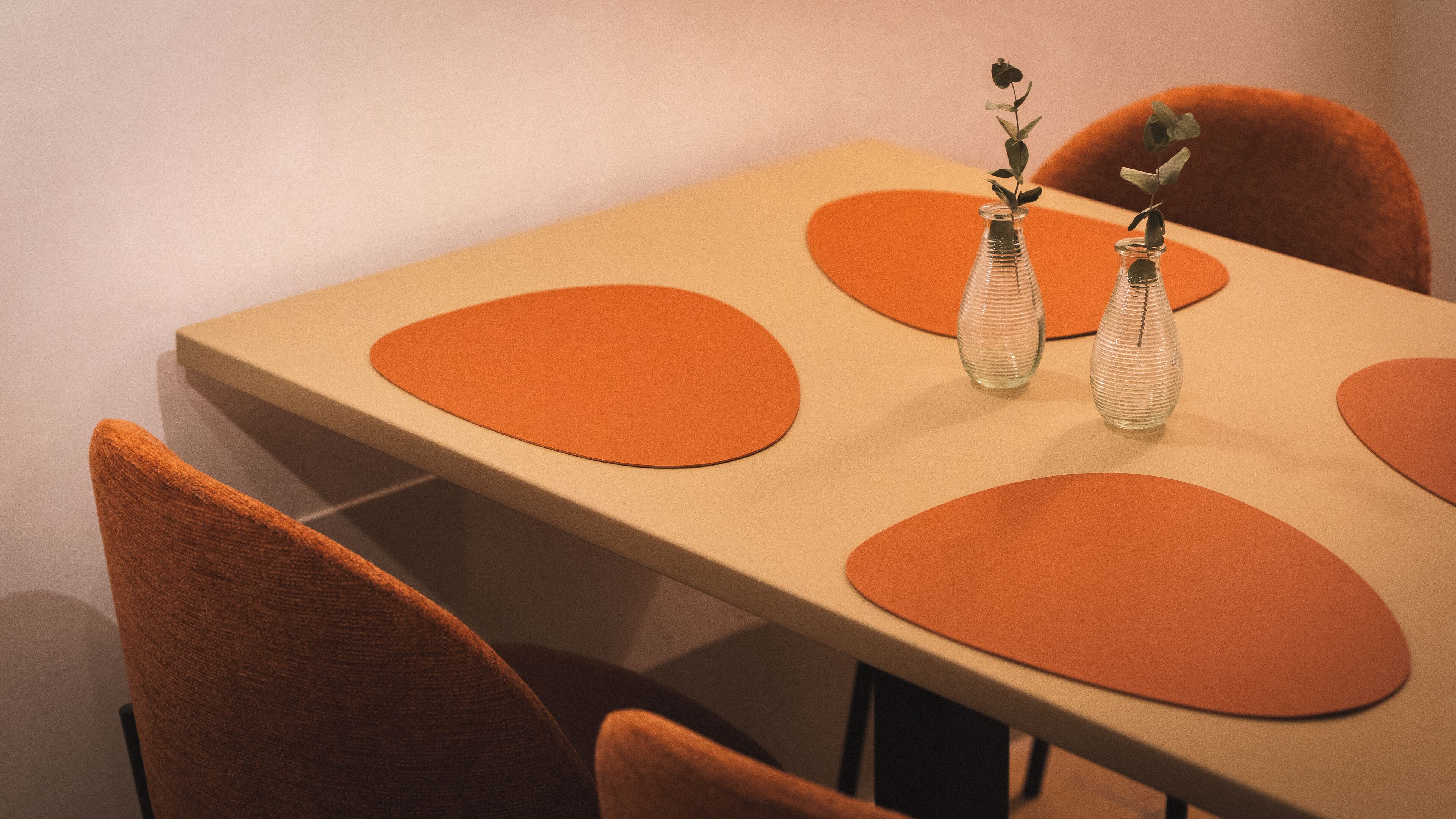 Une table avec des sets de table orange et deux vases en verre transparent contenant des plantes.