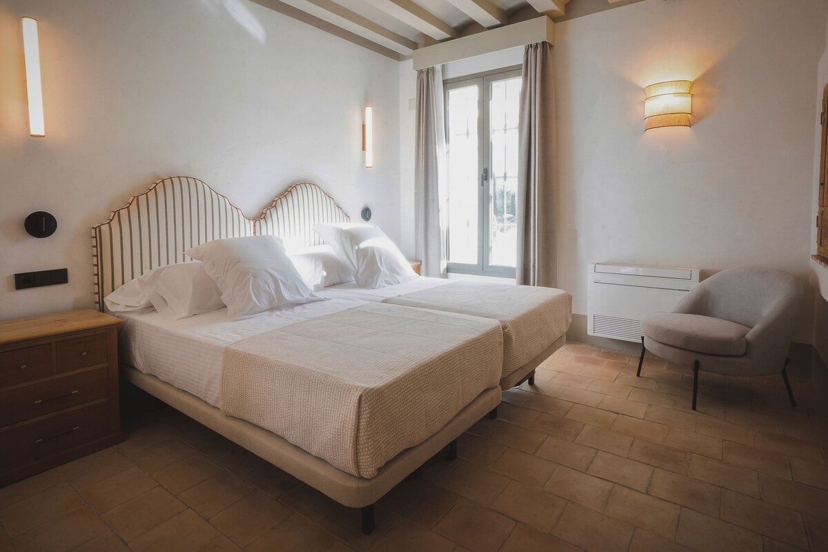 A bedroom with two beds, a nightstand, a chair, and a window with curtains.