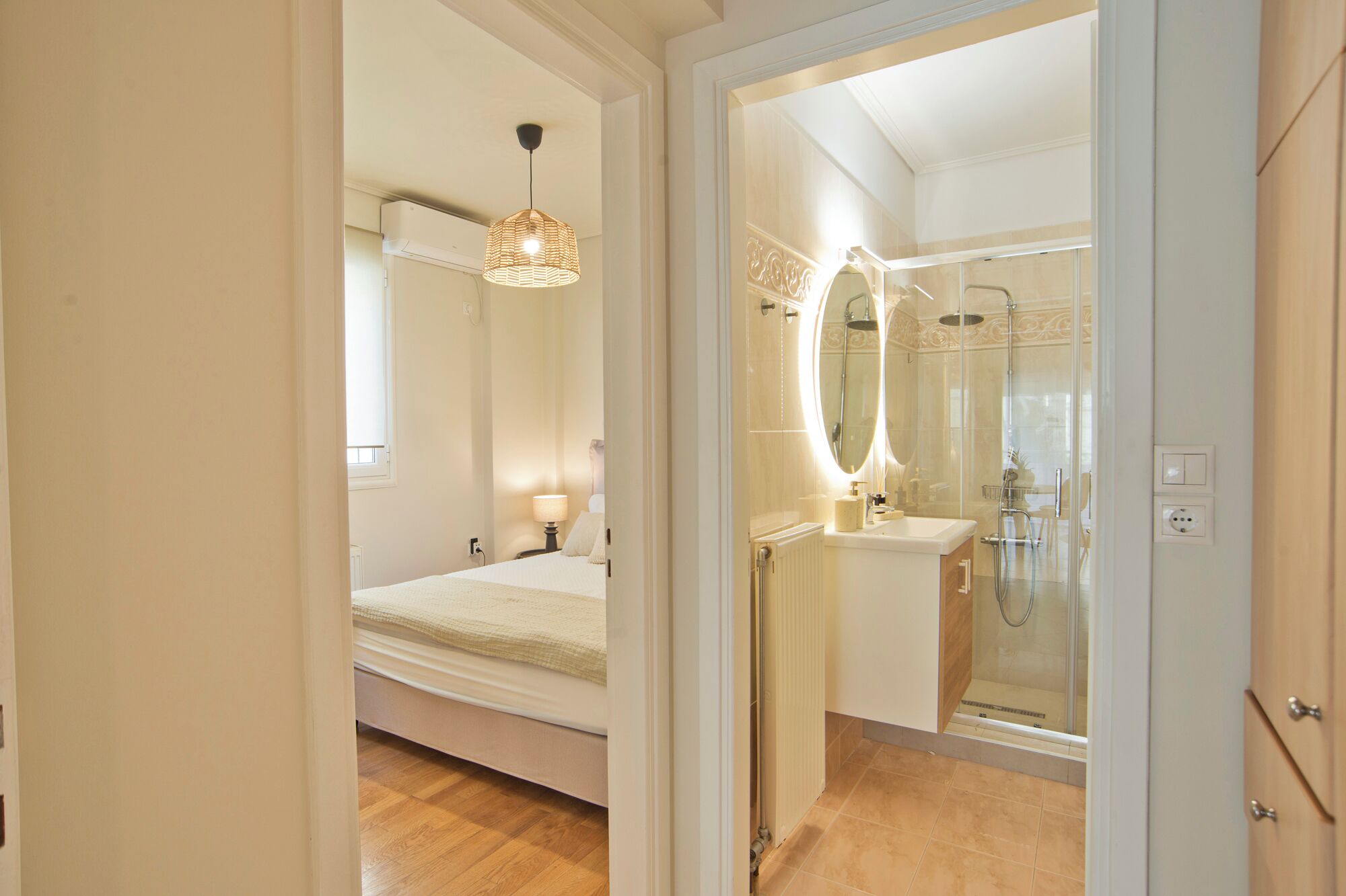 A modern bathroom with a glass shower enclosure, a vanity with a mirror, and a bed with a hanging light fixture.