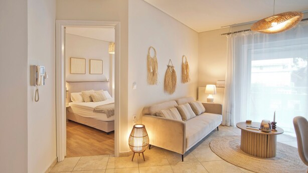 A modern hotel room with a bed, a sofa, a small table, and a lamp. There is a phone on the wall and a window with curtains. - Modern Beach Retreat 2BR in Coastal Palaio Faliro (Paleo Faliro)