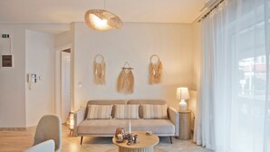 A modern living room with a sofa, a coffee table, and a hanging light fixture. - Modern Beach Retreat 2BR in Coastal Palaio Faliro (Paleo Faliro)
