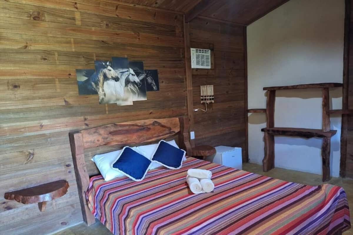 A wooden cabin room with a bed, a chair, and a wall-mounted picture of horses.