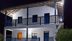 Um edifício de dois andares com varandas, um alpendre coberto e uma porta visível.