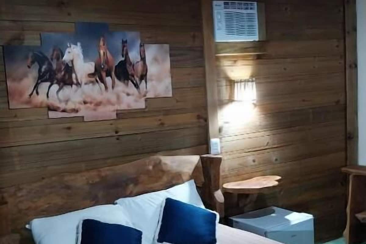 A wooden room with a bed, pillows, a painting, a table, and a chair.