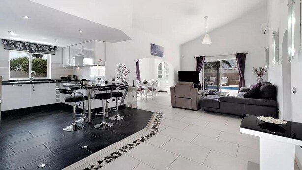 A modern kitchen with bar stools, a dining area with a white table and chairs, a living room with a sofa, and a pool view. - Exceptional 3 Bed Villa Malpas, Sleeps 6, H/pool (San Miguel de Abona)