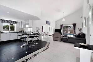 Una cocina moderna con taburetes de bar, un comedor con mesa y sillas blancas, una sala de estar con sofá y vistas a la piscina.