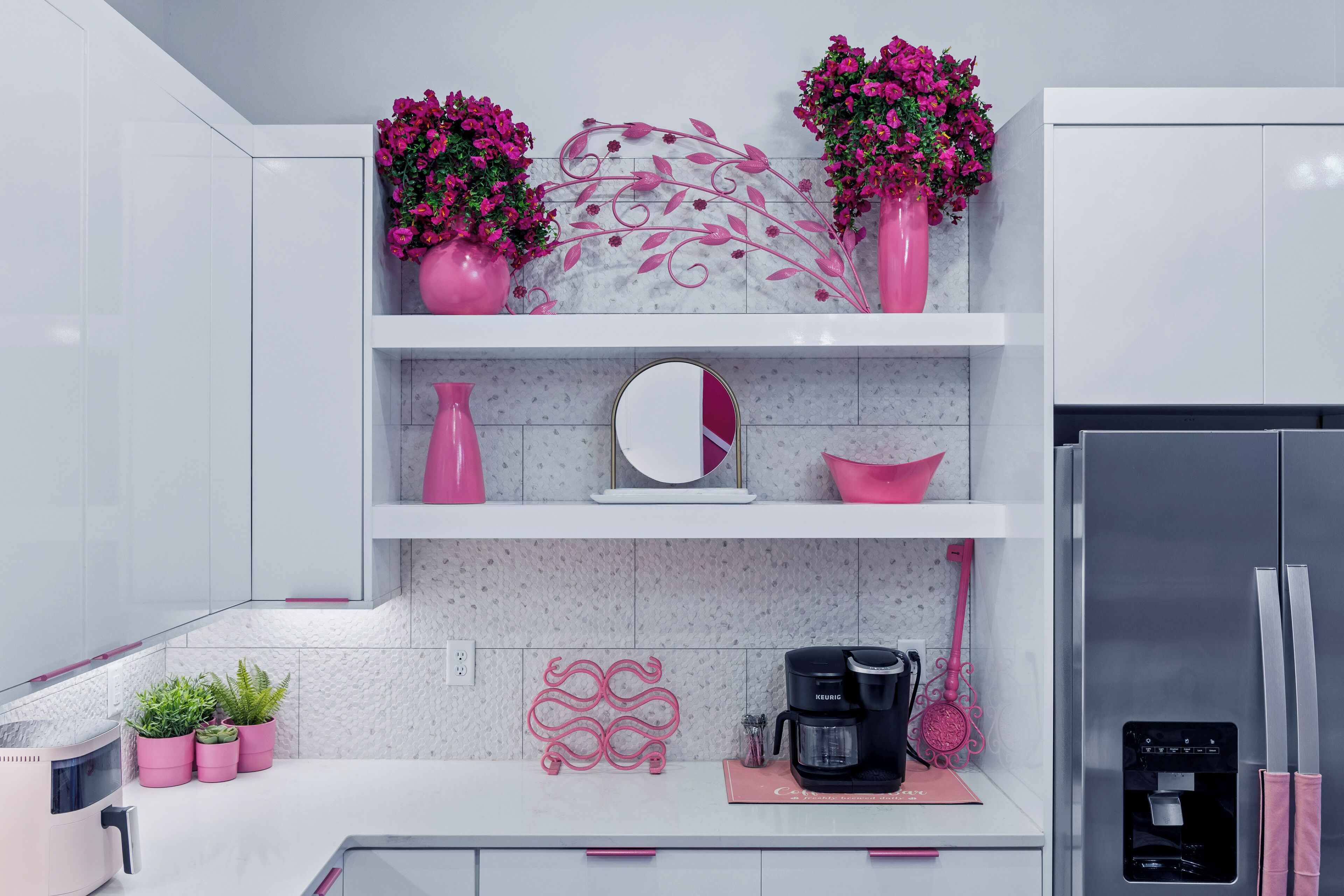 Een moderne keuken met witte kasten, roze accenten, een marmeren achterwand en een roestvrijstalen koelkast.