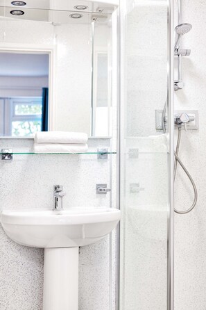 A bathroom with a glass shower enclosure, a white sink, and a glass shelf with a towel.