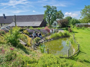 Un jardin avec un étang, une clôture en bois et un bâtiment doté d’un toit en pente.