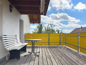 Une terrasse en bois avec un banc et une table, une clôture jaune et un bâtiment à l’extérieur blanc.