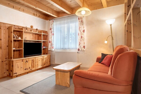 Un salon aux murs lambrés, avec un téléviseur, un canapé et une petite table.