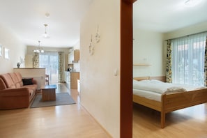 A modern room with a wooden bed, a sofa, a coffee table, and a kitchen area in the background.