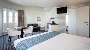 A hotel room with a bed, a desk with chairs, a sofa, a small kitchenette, and a TV mounted on the wall. - Relaxing Room with Kitchenette | Quick Access to Local Attractions (Oostende)