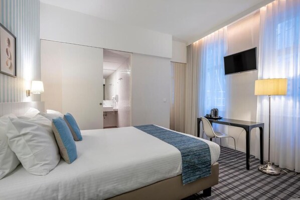 Una habitación de hotel con una cama, un escritorio, una silla, un televisor y una lámpara.