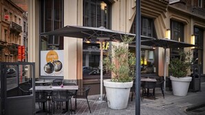 An outdoor cafe with tables and chairs, a large planter, and a sign advertising coffee. - Peaceful Stay Close to the Breathtaking Beach: Scenic Afternoon Walks | 3 Rooms (Oostende)