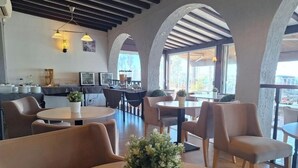 Ein modernes Restaurant mit runden Tischen, bequemen Sitzgelegenheiten und großen Fenstern.