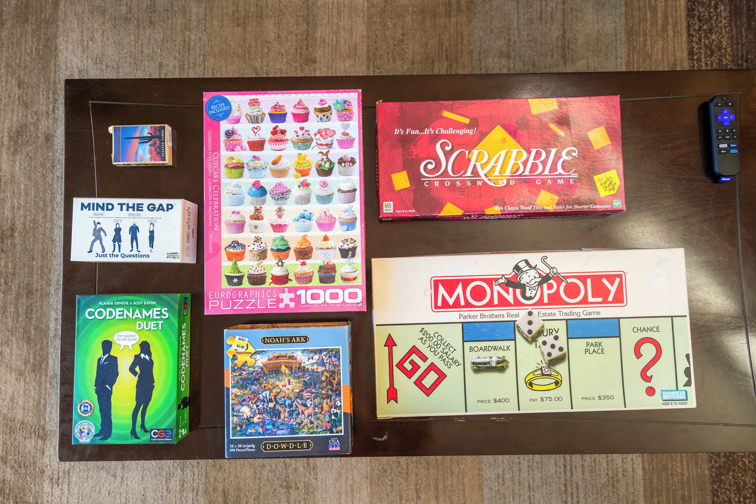Puupöydällä on useita erilaisia lautapelejä, kuten Scrabble, Monopoly ja Codenames Duet.