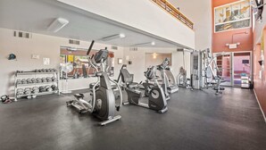 Une salle de sport équipée de divers appareils d’exercice, de supports pour les poids et d’un mur recouvert de miroirs.