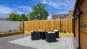 Un patio al aire libre con cerramiento de madera, una mesa de piedra y mobiliario de mimbre negro.