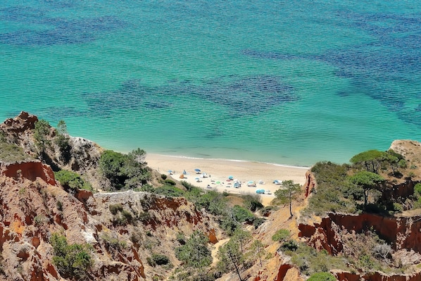 A coastal landscape with a beach, rocky cliffs, and clear turquoise water.