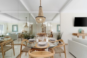 A modern dining area with a glass table, wooden chairs, and a chandelier.