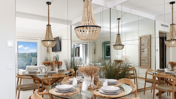 A dining area with a glass table, wooden chairs, and a chandelier.