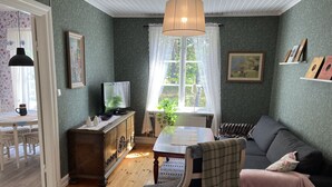 A cozy living room with a wooden floor, a sofa, a television, and a dining area with a table and chairs.