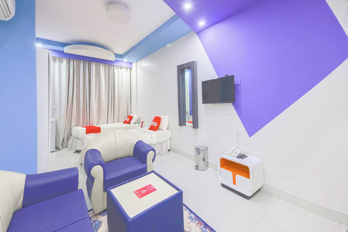 A hotel room with a modern design, featuring a sofa set, a small table, a TV mounted on the wall, and a reception desk.