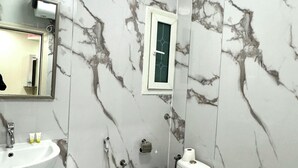 A bathroom with a sink, toilet, and bidet, all against a marble wall. - Dancenter Muscat Holiday Luxury Stay (Seeb)