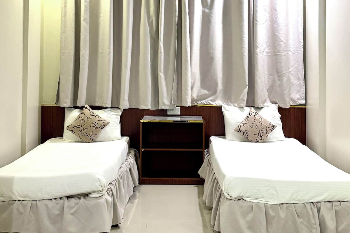 A hotel room with two single beds, a wooden headboard, a small table, and a ceiling light fixture.