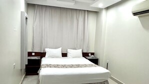 A modern hotel room with a large bed, a nightstand, a wardrobe, and a ceiling with recessed lighting. - Dancenter Muscat Holiday Luxury Stay (Seeb)
