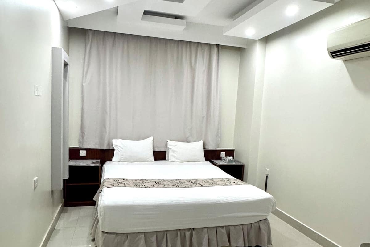 A modern hotel room with a large bed, a nightstand, a wardrobe, and a ceiling with recessed lighting.