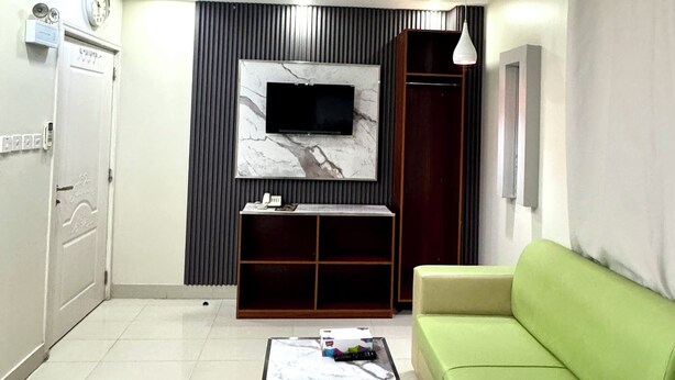 A modern living room with a flat-screen TV mounted on a marble wall, a green sofa, a beige ottoman, and a tiled floor. - Dancenter Muscat Holiday Luxury Stay (Seeb)