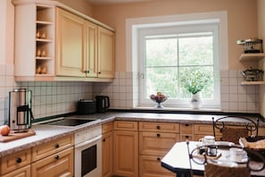 A kitchen with wooden cabinets, a window with a view, a coffee maker, and a bowl of fruit on the windowsill. - Holiday Home 'Kleinod' with Mountain View, Shared Terrace and Wi-Fi (Naumburg)