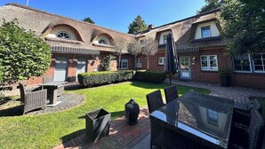 Une cour avec un bâtiment à toit de chaume, une terrasse pavée et du mobilier d’extérieur.