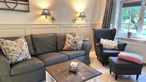 Un salon avec un canapé gris, un fauteuil assorti, une table basse en bois et deux lampes fixées au mur.