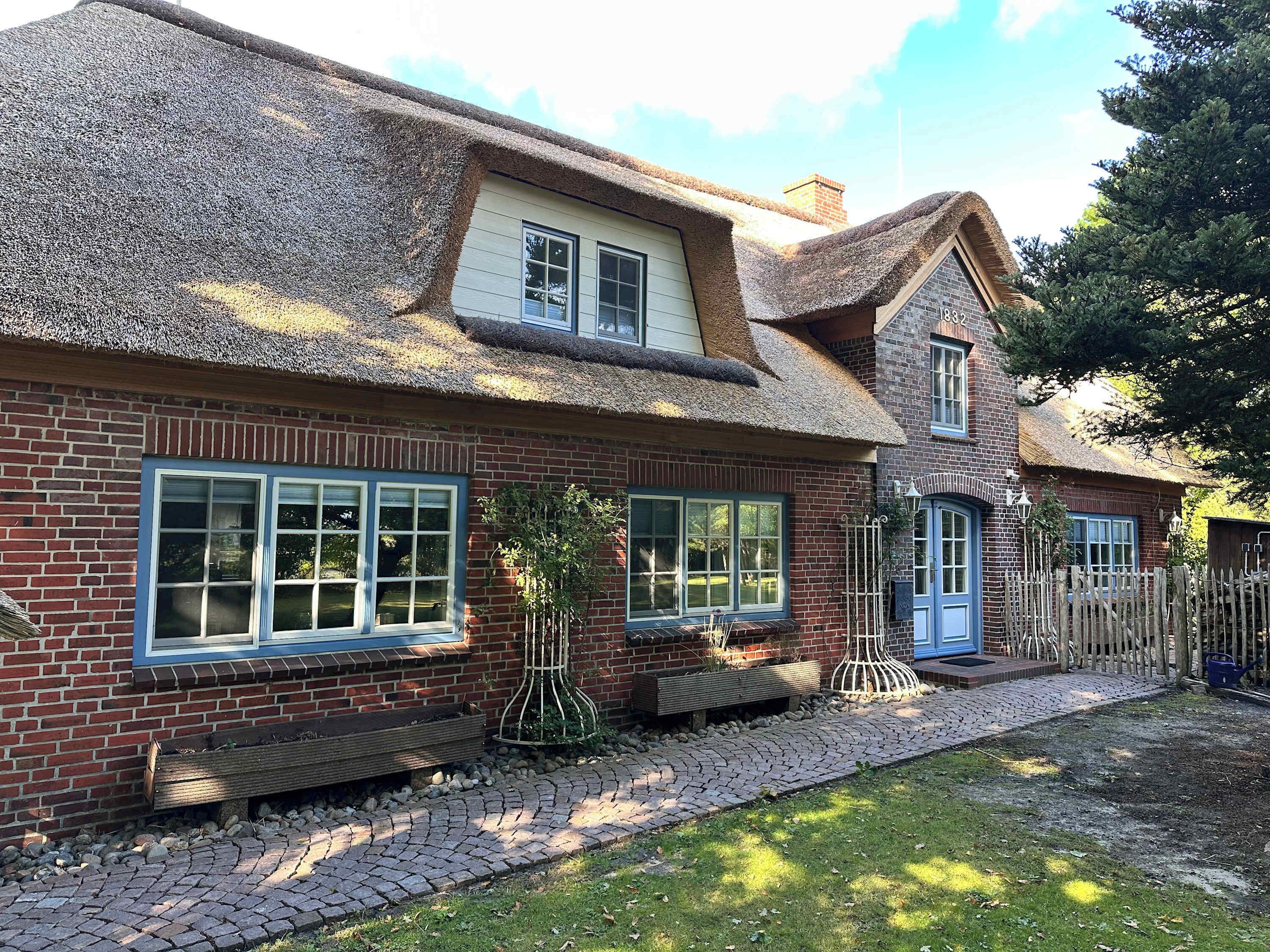 A two-story brick house with a thatched roof, a small front porch, and a paved driveway.
