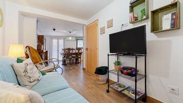 A living room with a sofa, TV, and shelves with books and plants.