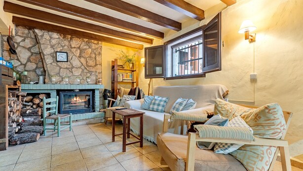 Una sala de estar acogedora con pared de piedra, chimenea, sofá y televisor montado en la pared.