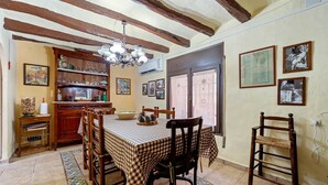 Un comedor con mantel a cuadros, sillas de madera, una araña y un aparador con cristalería.